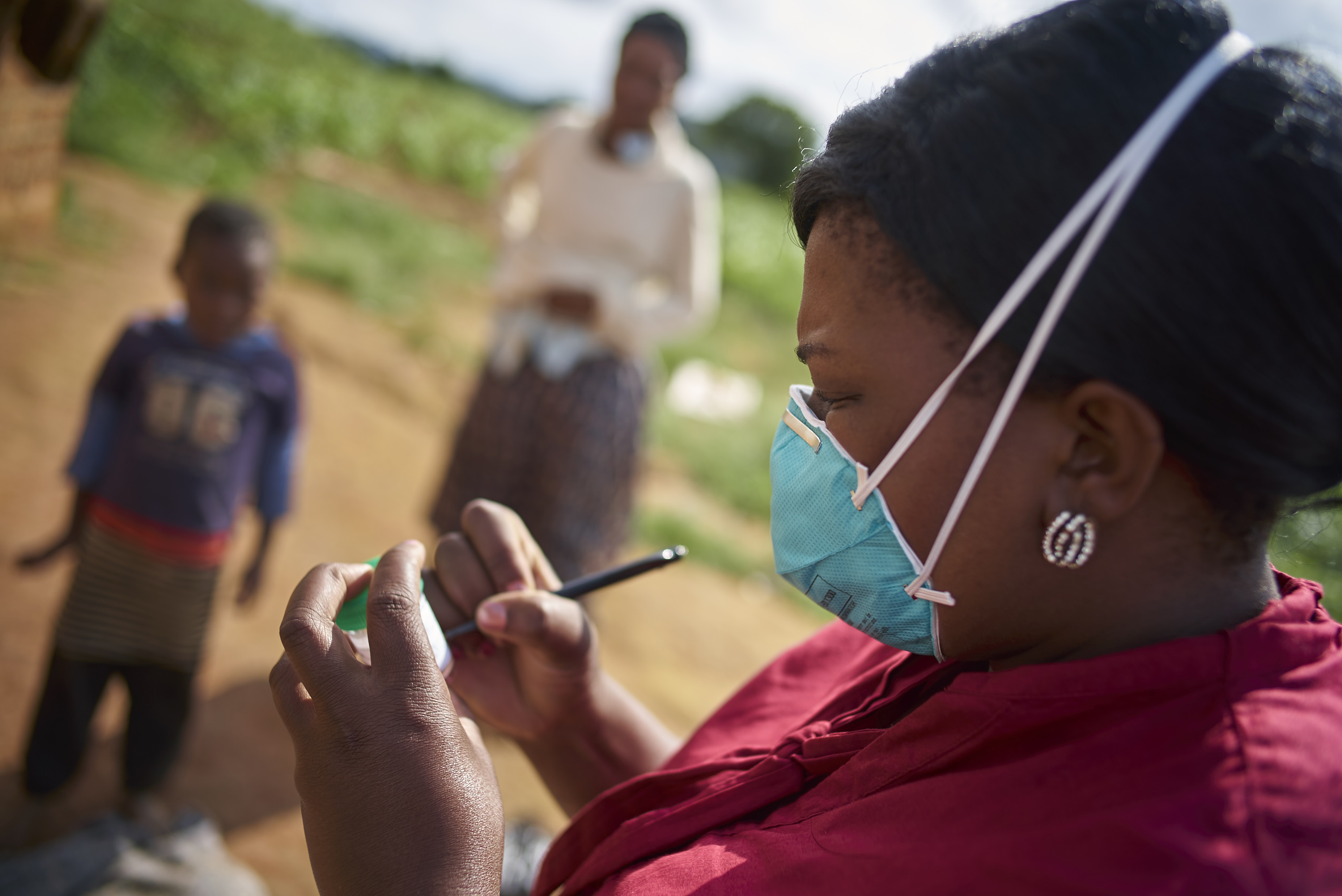 A woman writing something on a bottle while wearing a clinical mask and standing near presumptive patients.